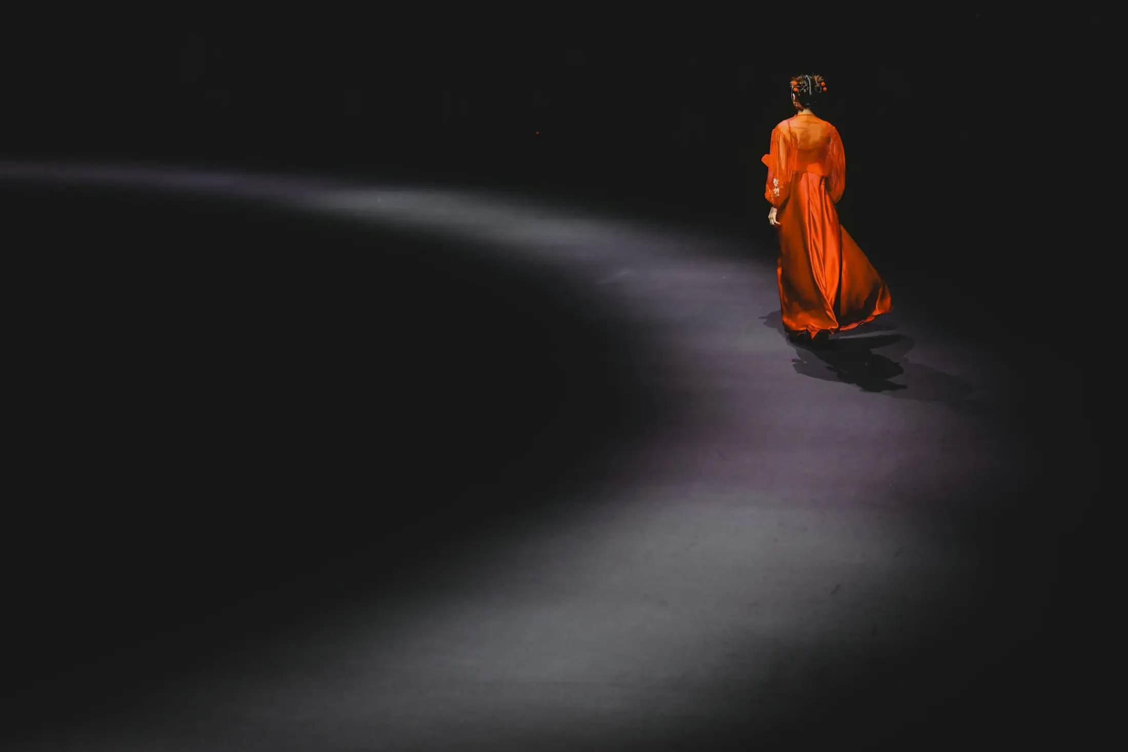 Model in orangem Kleid auf einem dunklen Laufsteg in Bewegung