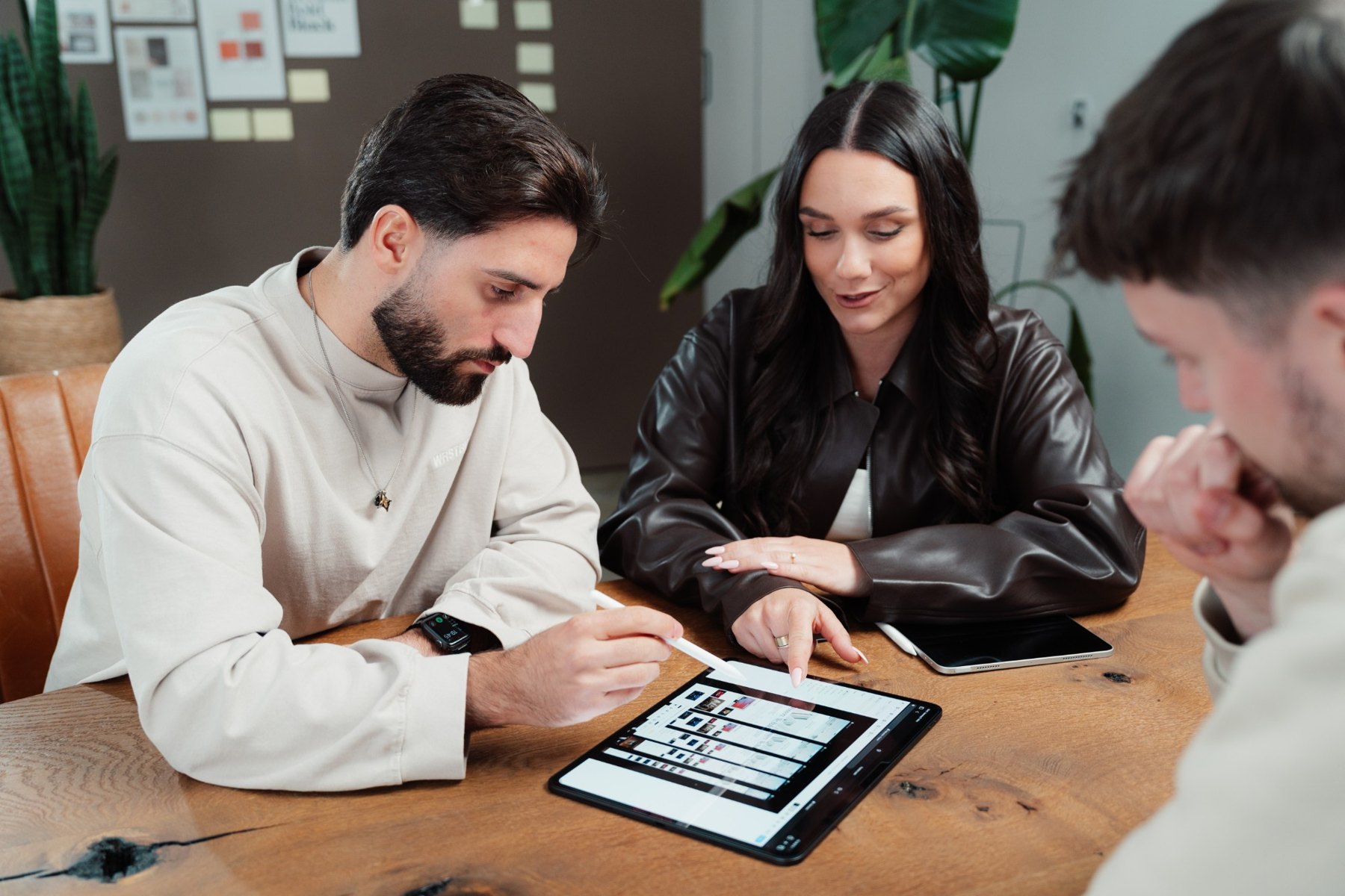 Drei Personen aus dem NextPercent-Team sitzen an einem Holztisch und besprechen auf einem Tablet einen Seitenentwurf